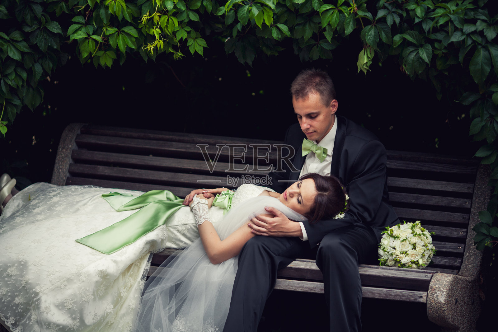 婚礼上,新人躲在拱形树叶下的长凳上。自然照片摄影图片