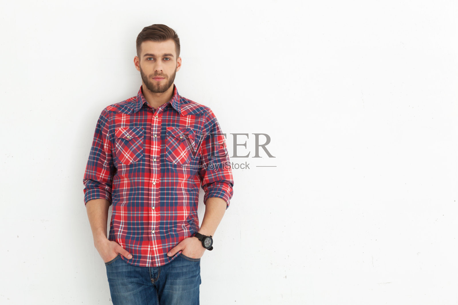 一个英俊的年轻人靠着白墙站着。照片摄影图片