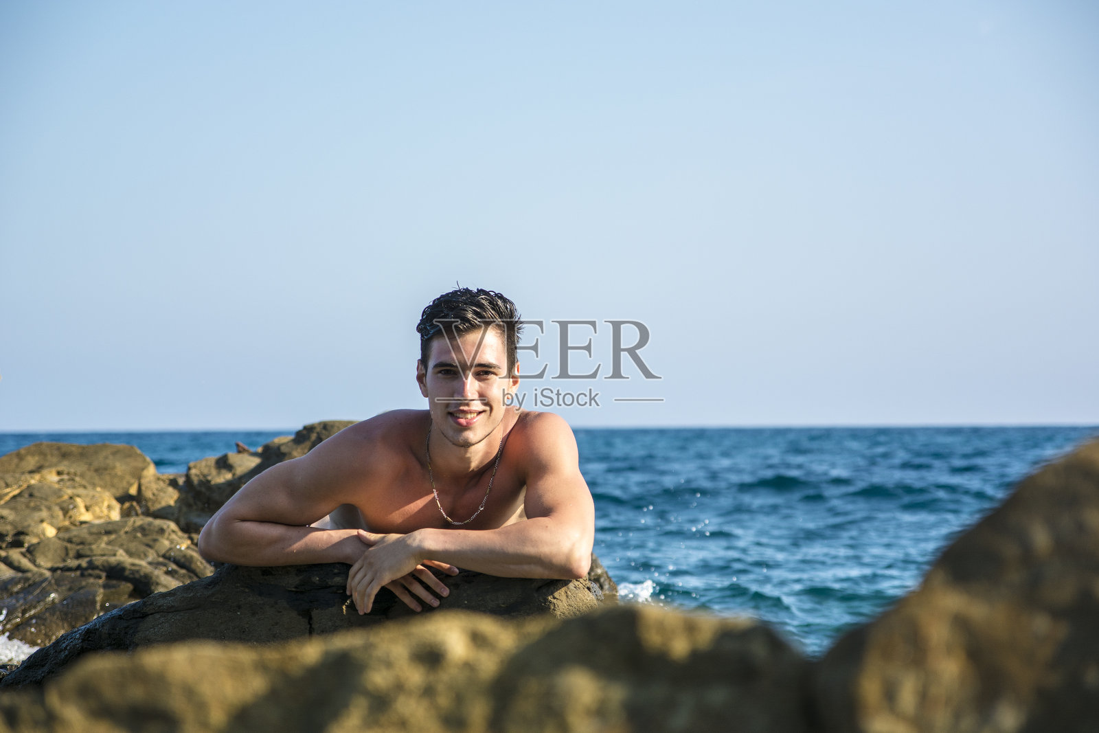 年轻的赤膊运动员靠在海边的岩石上照片摄影图片