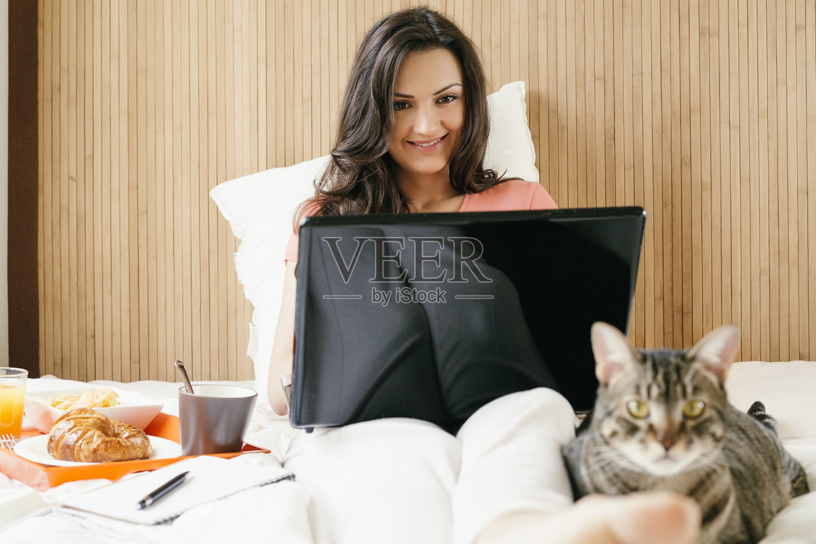 一个女人一边用笔记本电脑工作一边吃早餐。照片摄影图片