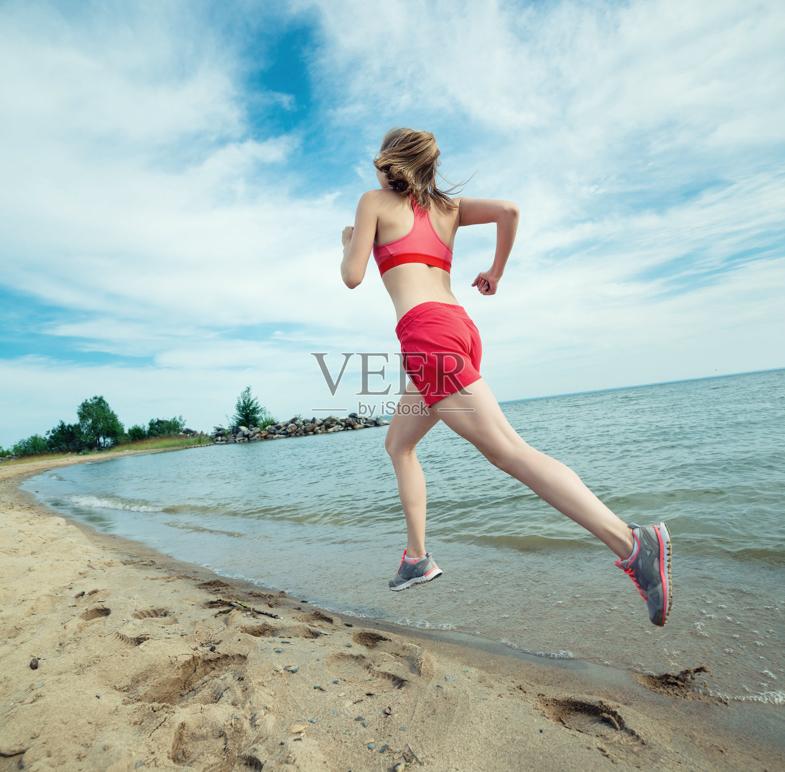 年轻的女士在阳光明媚的夏日沙滩上奔跑。锻炼照片摄影图片