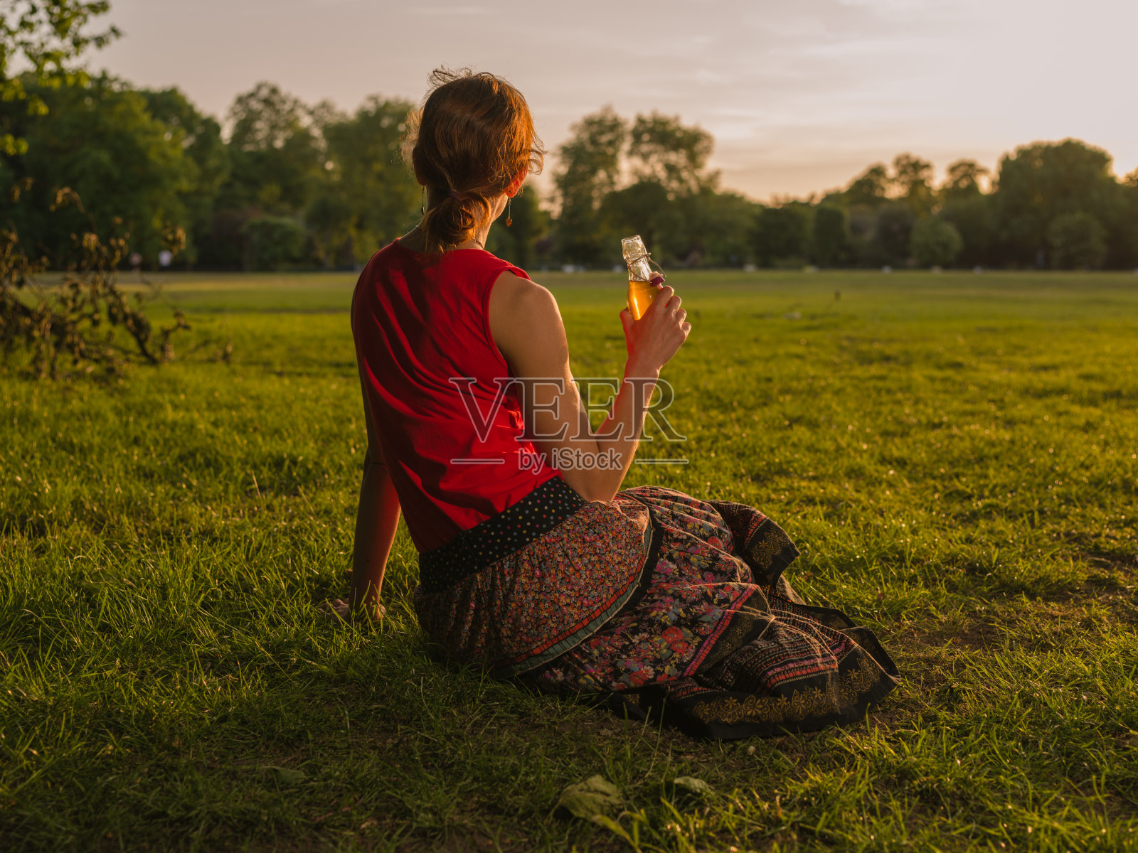 在公园里喝酒欣赏日落的女人照片摄影图片