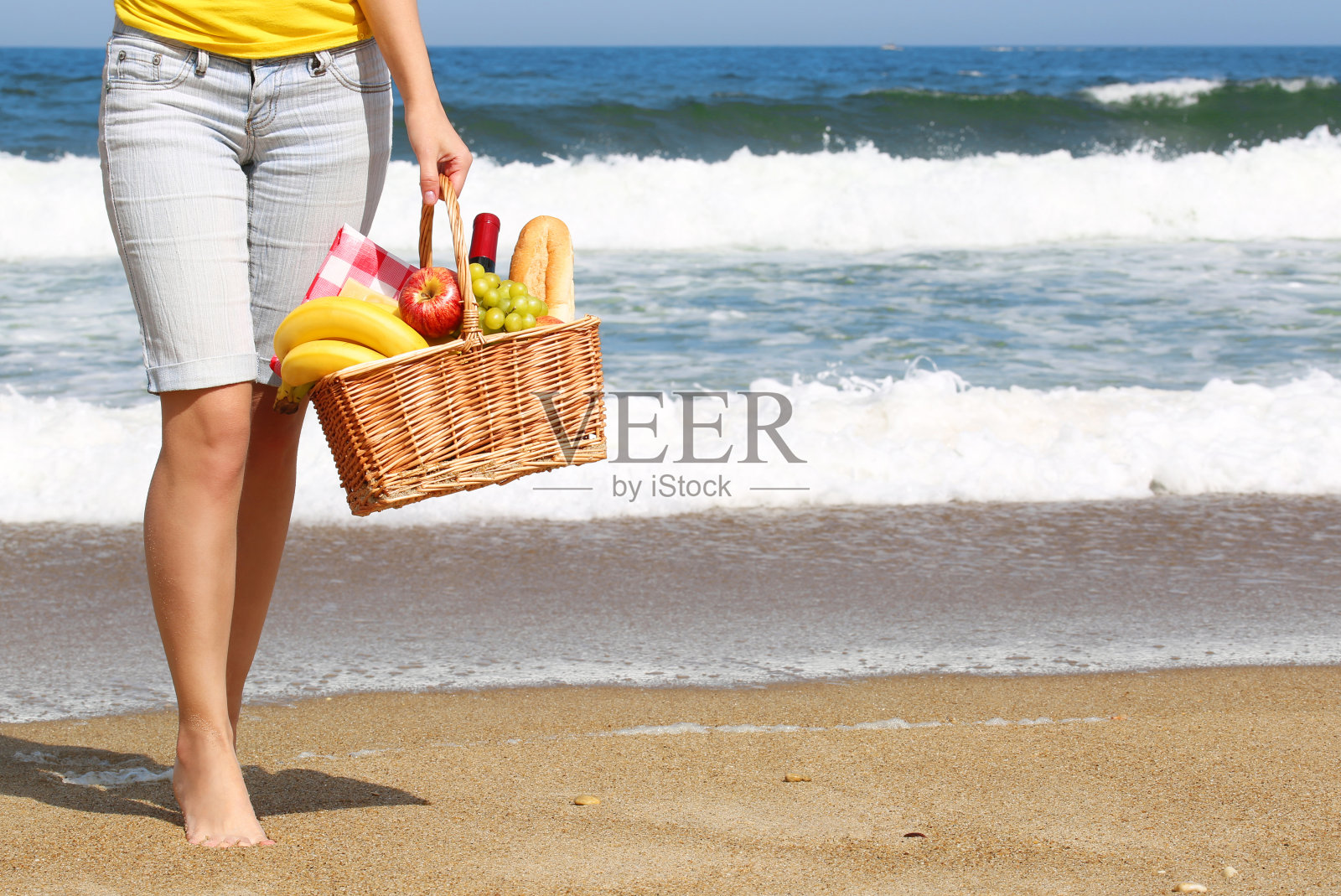 海滩野餐。女性的腿和篮子与食物照片摄影图片