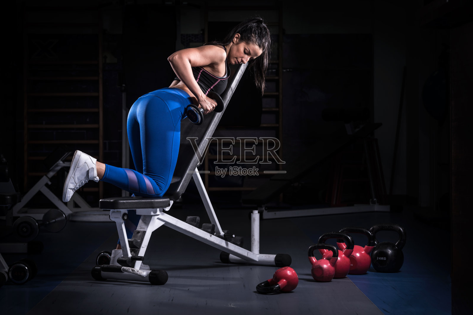 穿着运动服在健身房举哑铃的女性健美运动员照片摄影图片