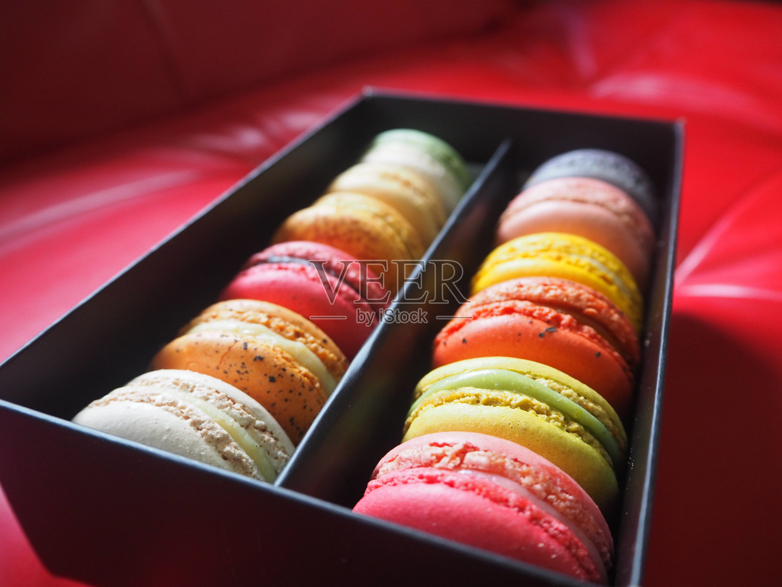 红色沙发上的盒子里有五颜六色的马卡龙照片摄影图片