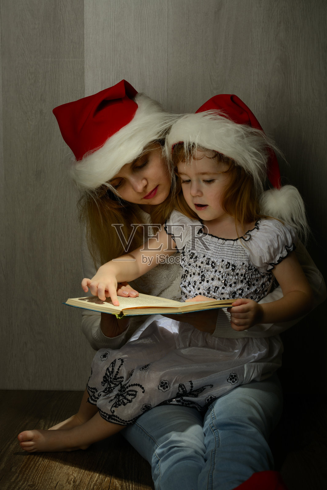 小女孩和妈妈在圣诞老人的帽子里看书照片摄影图片