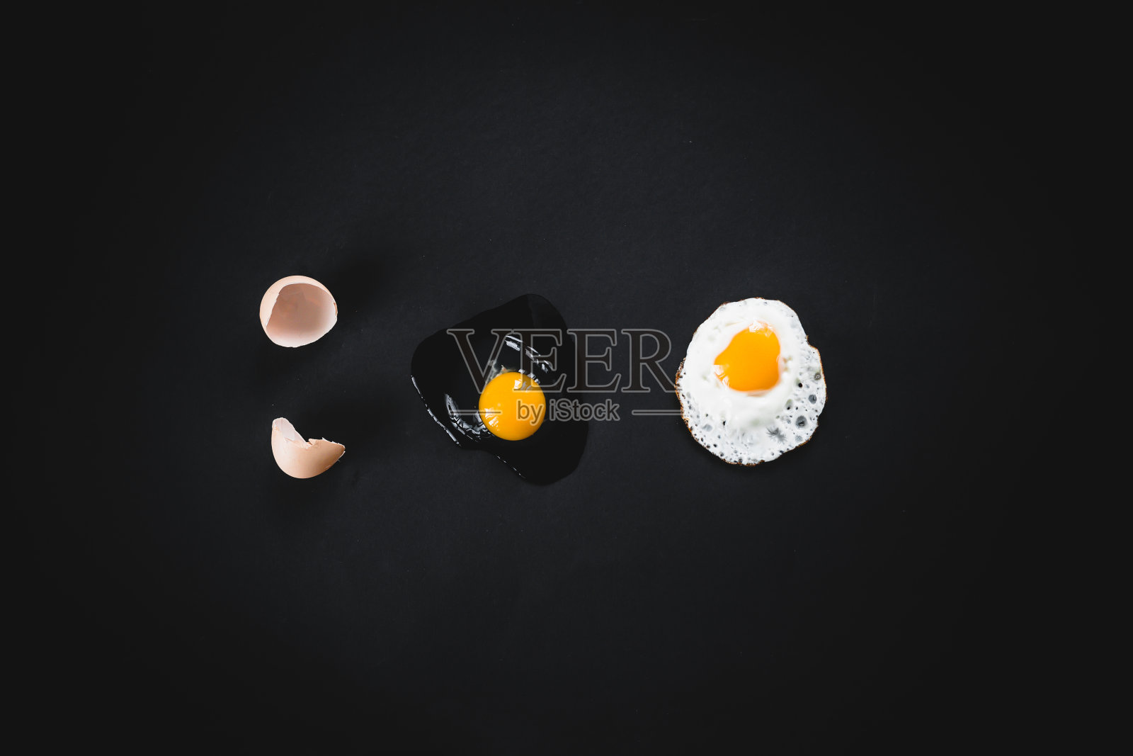 在黑色的背景上煎生的破鸡蛋。理念:从原料到成品的过程。照片摄影图片