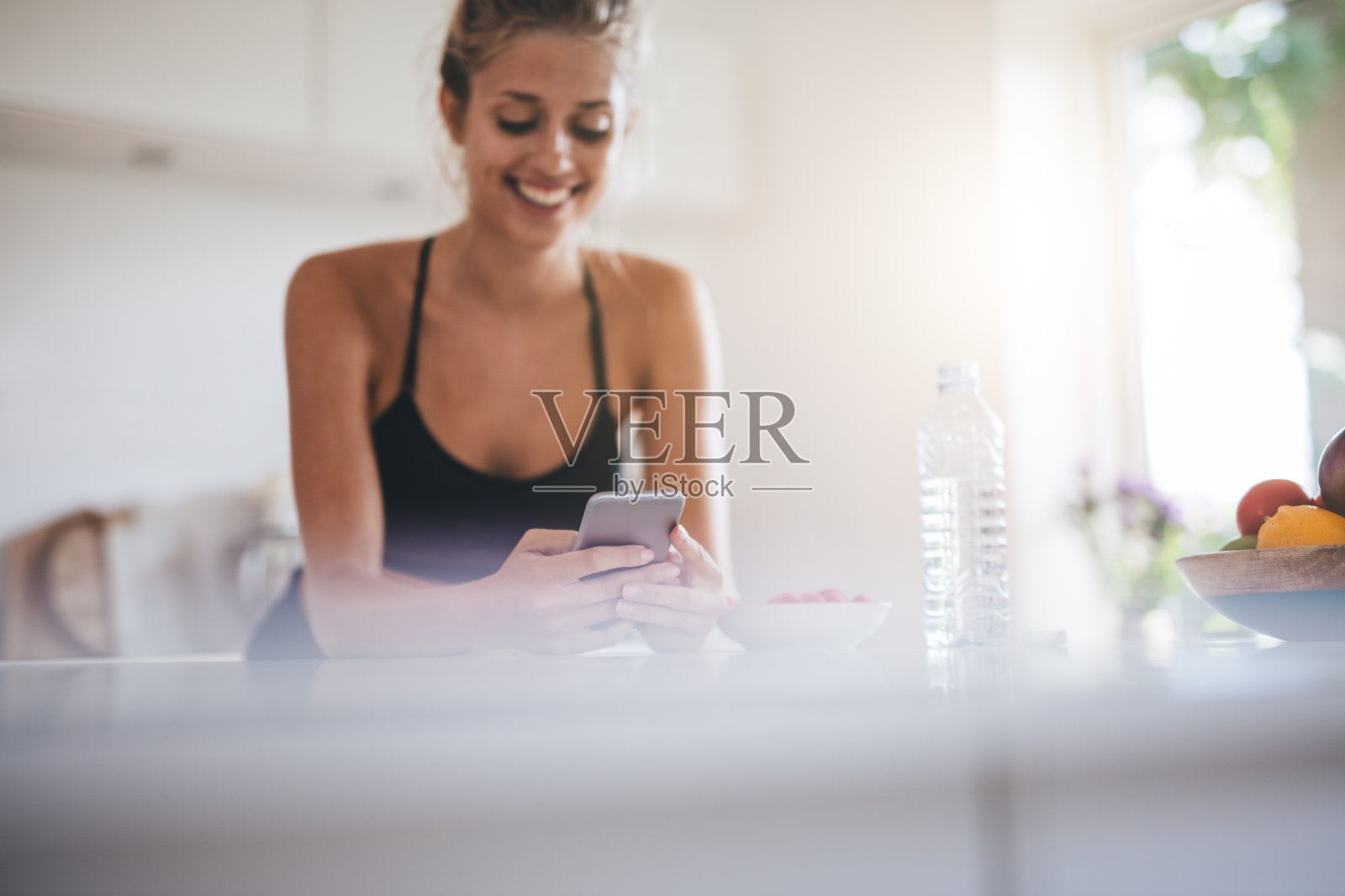 微笑的女人吃早餐和使用手机在厨房照片摄影图片