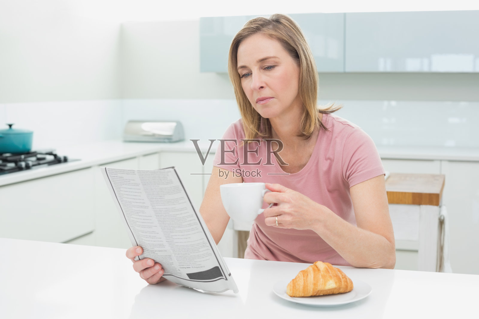 专注的女人一边看报纸一边在厨房喝咖啡照片摄影图片
