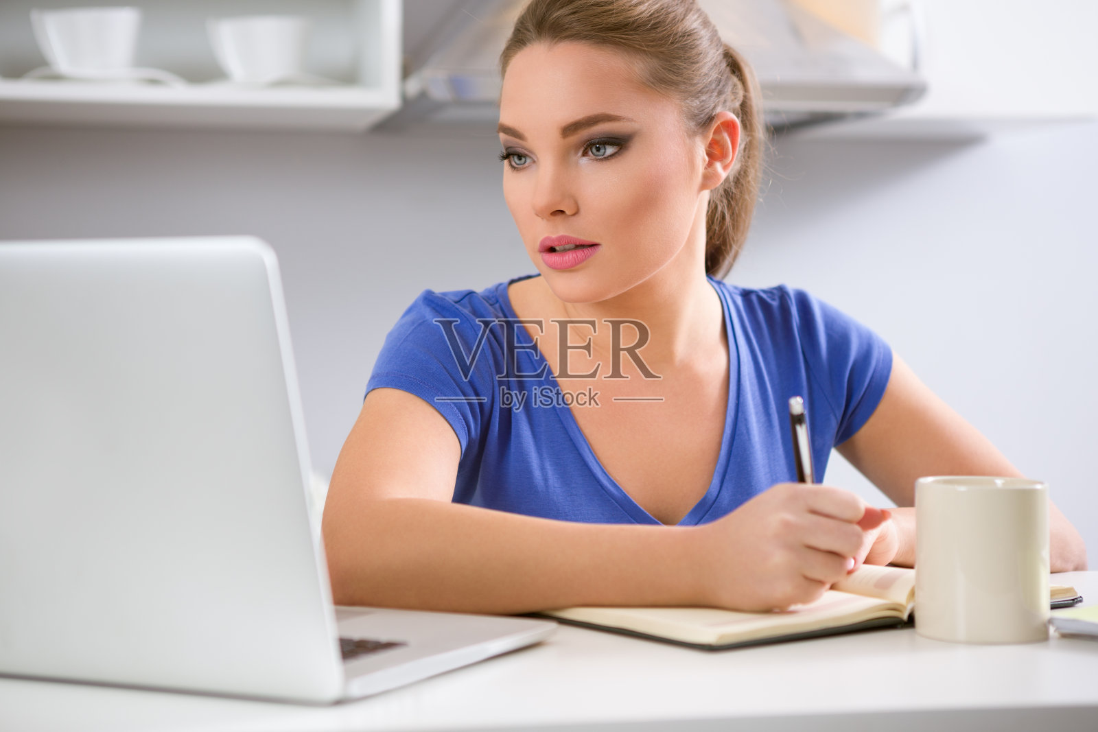 在厨房里喝着咖啡看笔记本电脑的女人照片摄影图片