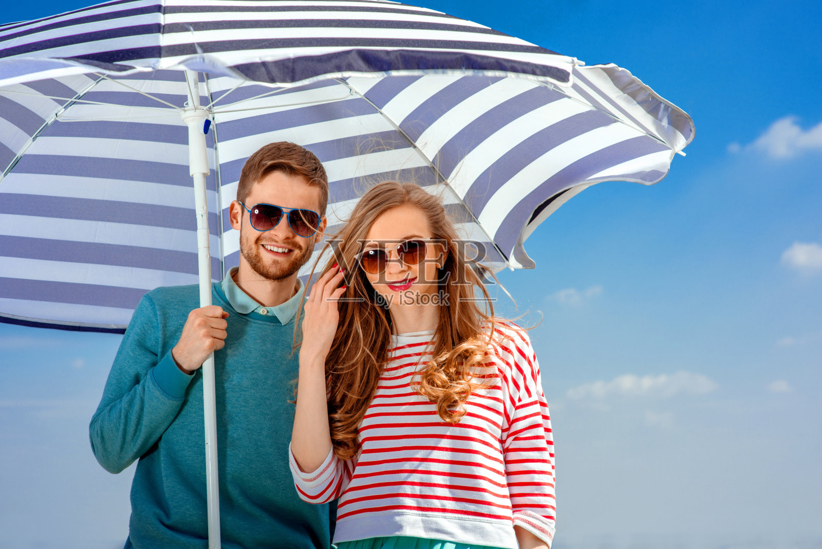 蓝天背景下,伞下笑眯眯的年轻情侣照片摄影图片