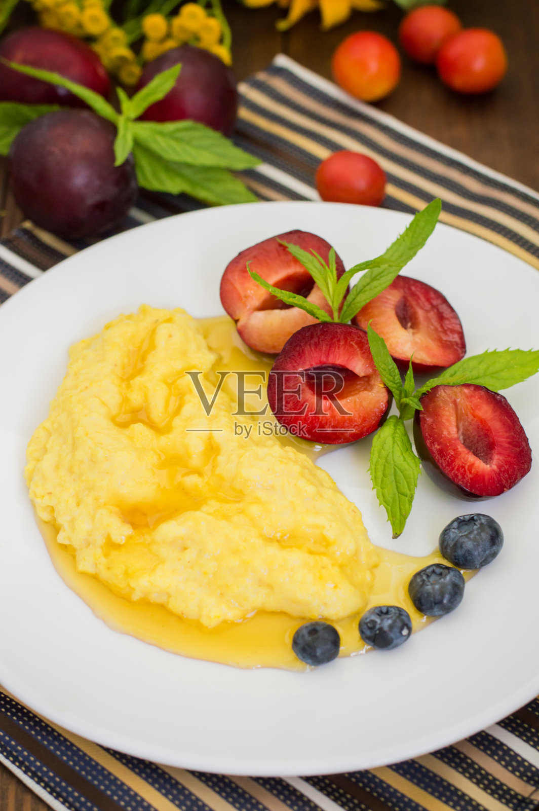 玉米粥配蜂蜜,李子,蓝莓和樱桃。木照片摄影图片