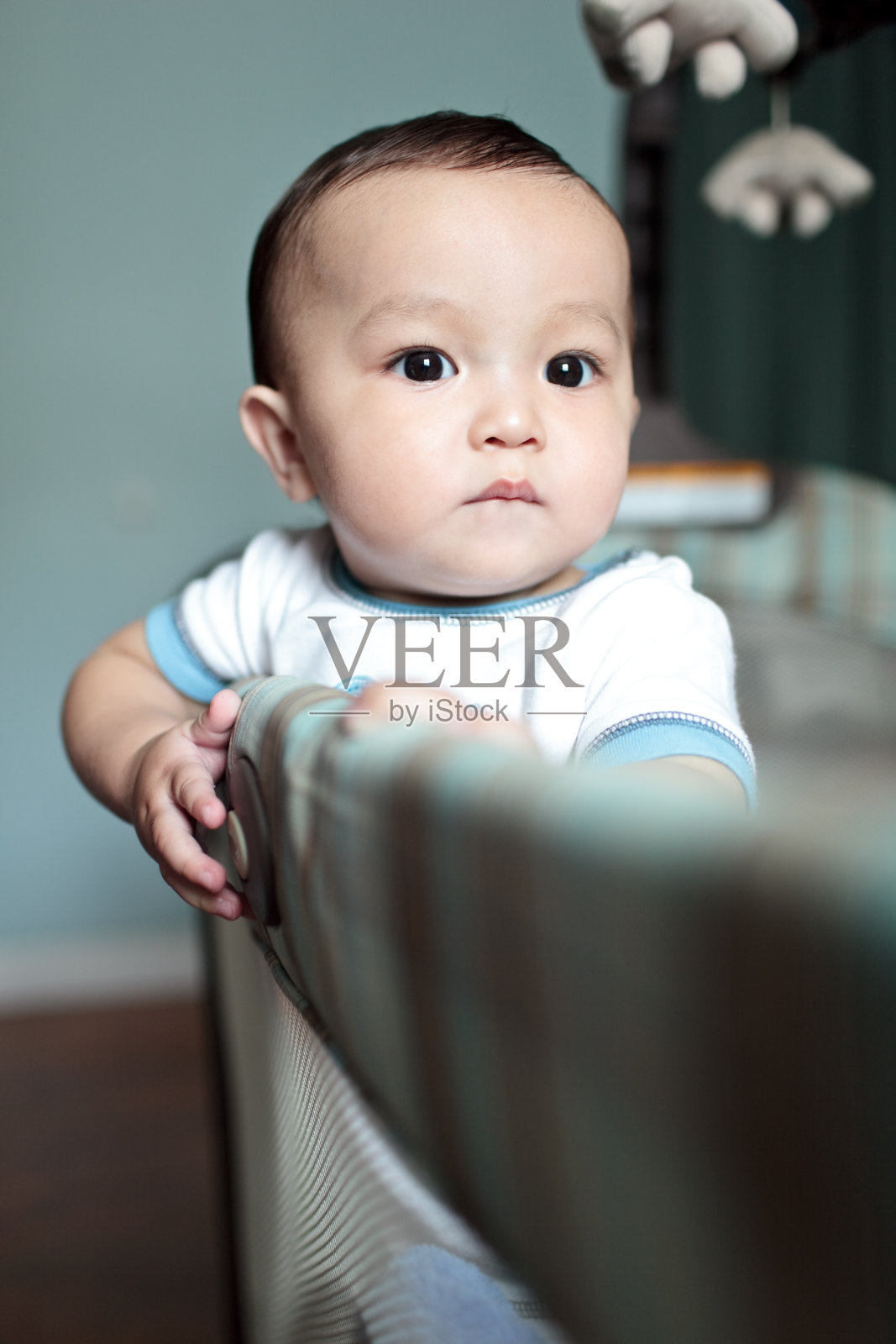 可爱的小男孩站在他的婴儿床旁照片摄影图片