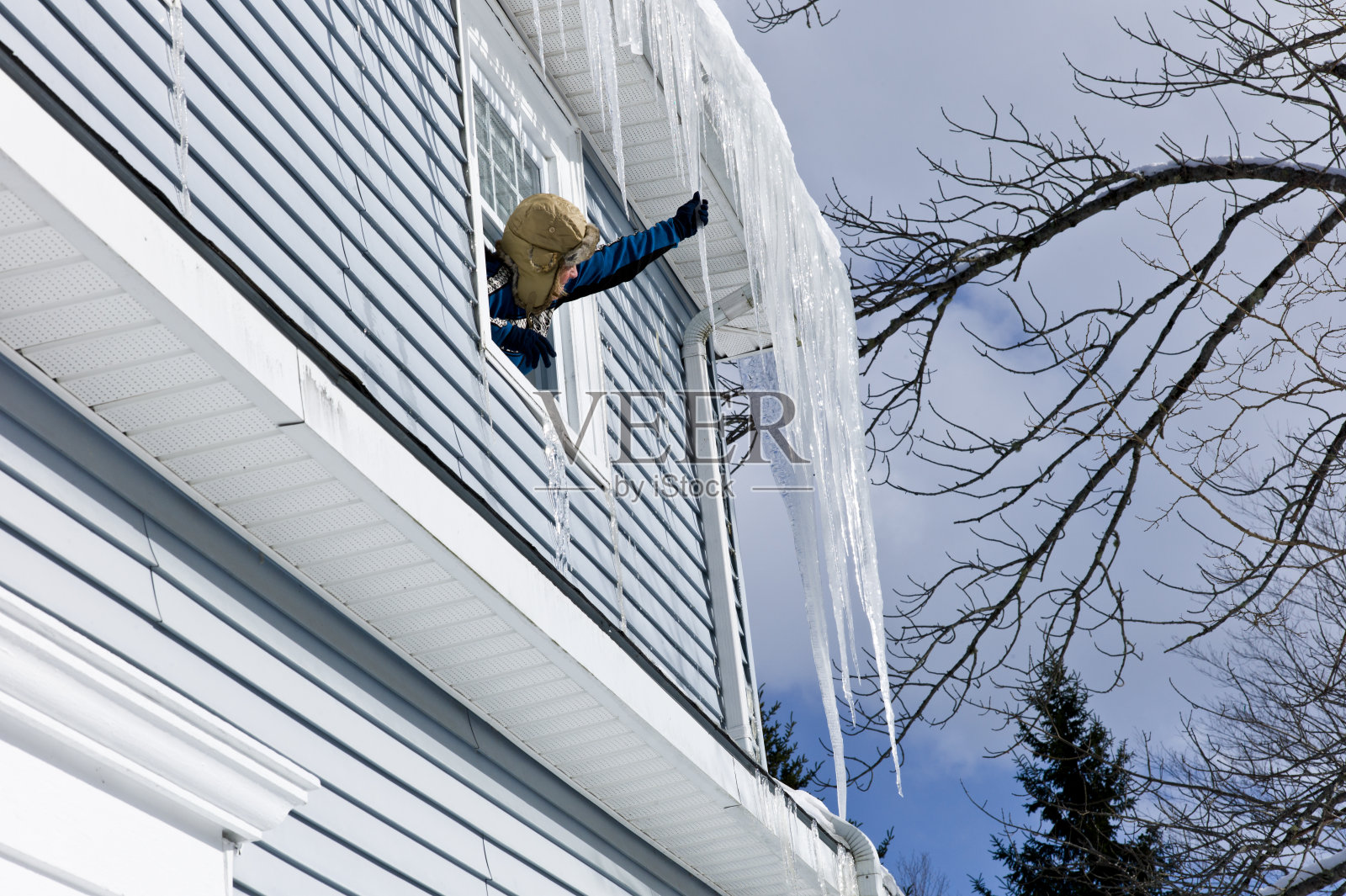 成熟的女人斜靠在窗外打破冰柱。照片摄影图片