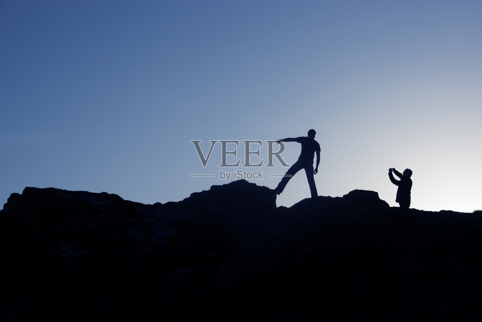 两个人站在岩石上的剪影。照片摄影图片