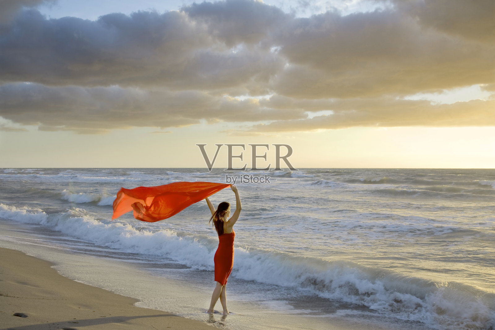 女人在日落的海滩上拿着红围巾风照片摄影图片