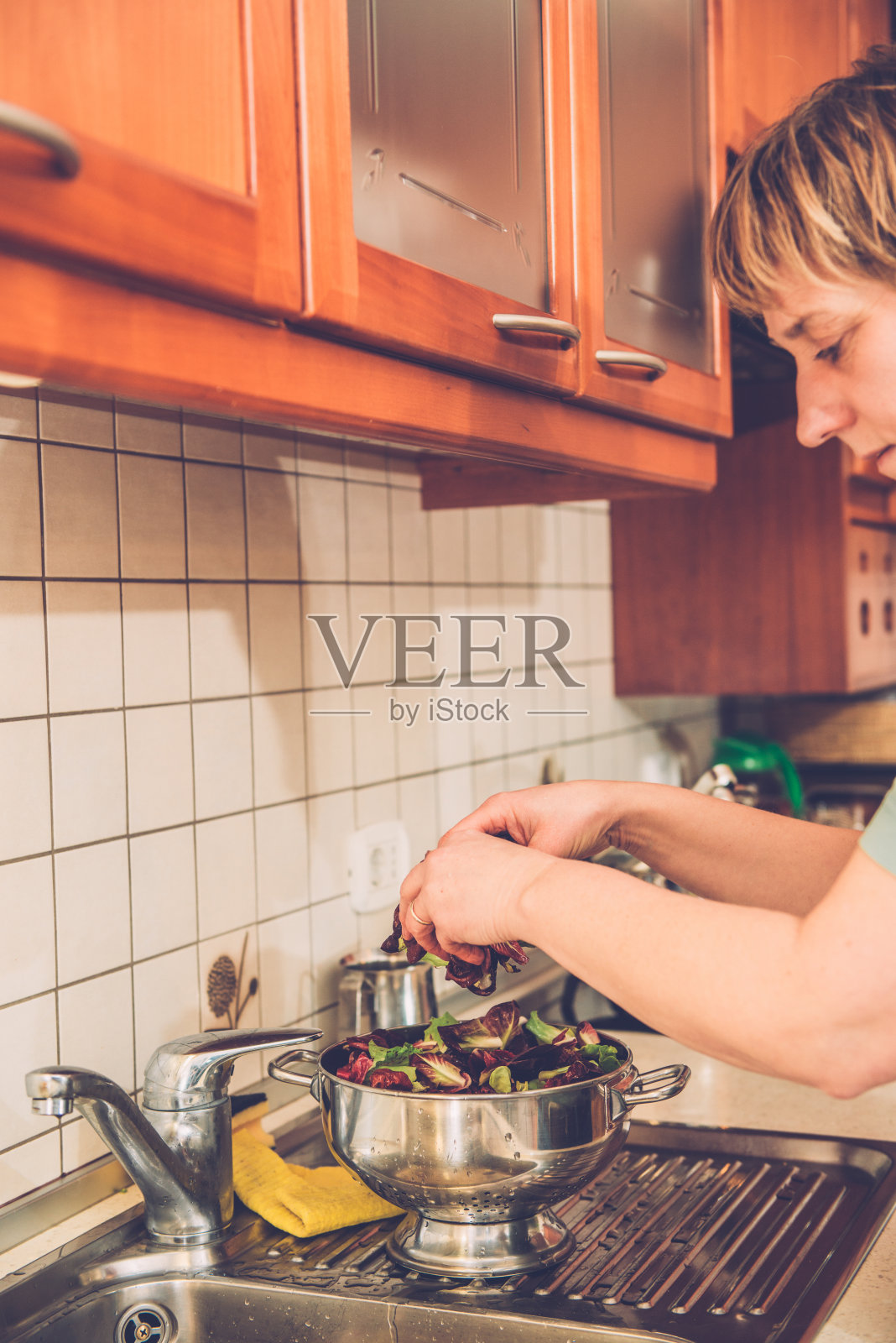 穿着牛仔裤的女人在水槽里洗沙拉,家庭厨房,欧洲照片摄影图片