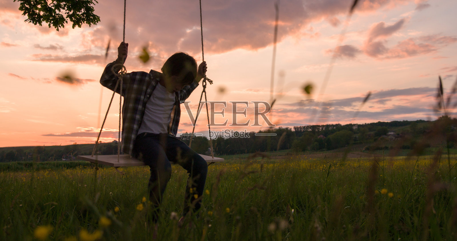 男孩在操场荡秋千在日落照片摄影图片