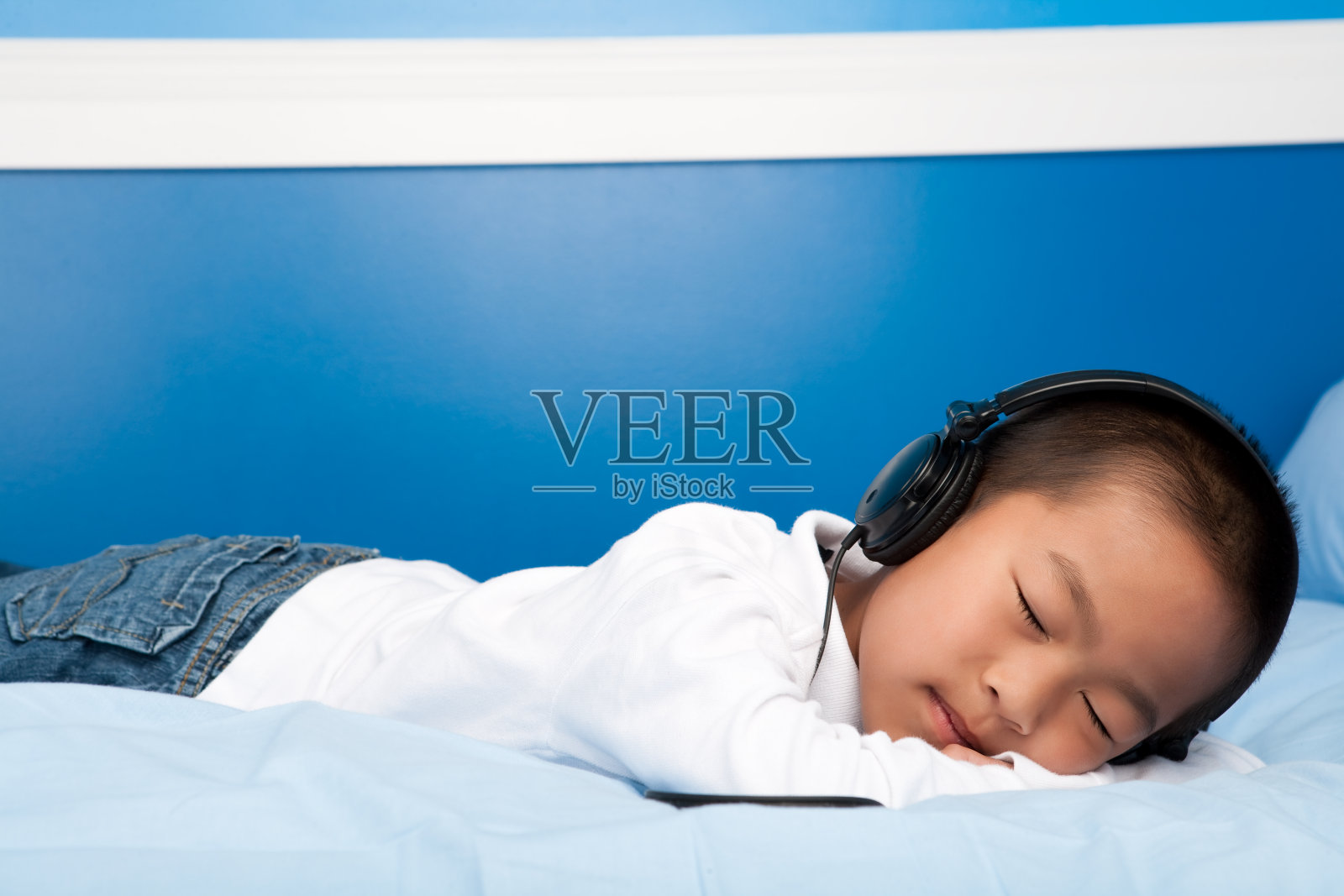 亚洲男孩在床上听耳机照片摄影图片
