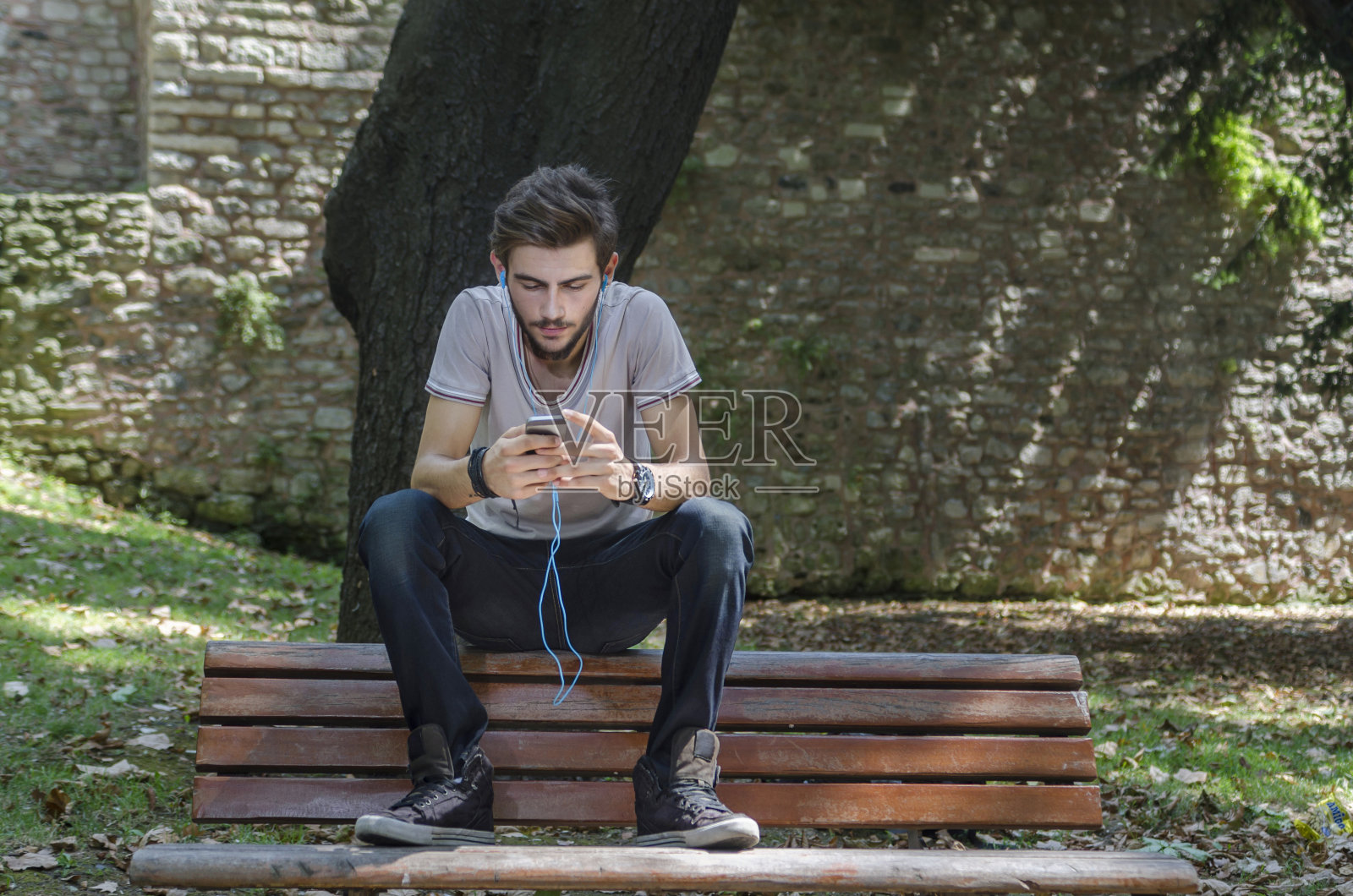 微笑的年轻人一边发短信一边看他的智能手机照片摄影图片