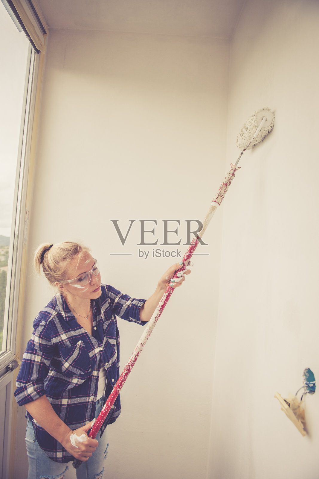 年轻的金发女人正在用油漆滚筒刷墙照片摄影图片