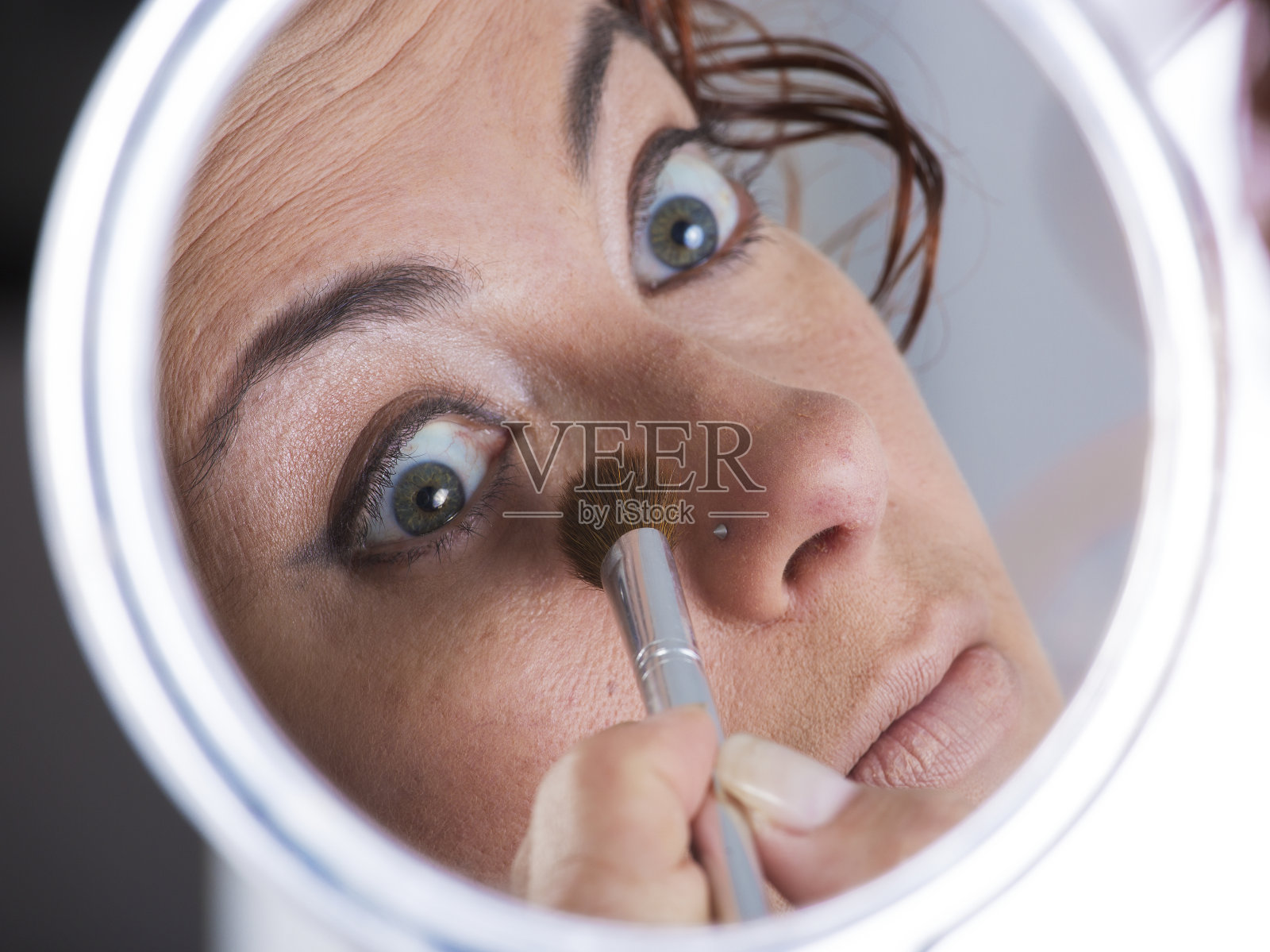 女人用化妆刷在化妆镜里照出的脸照片摄影图片