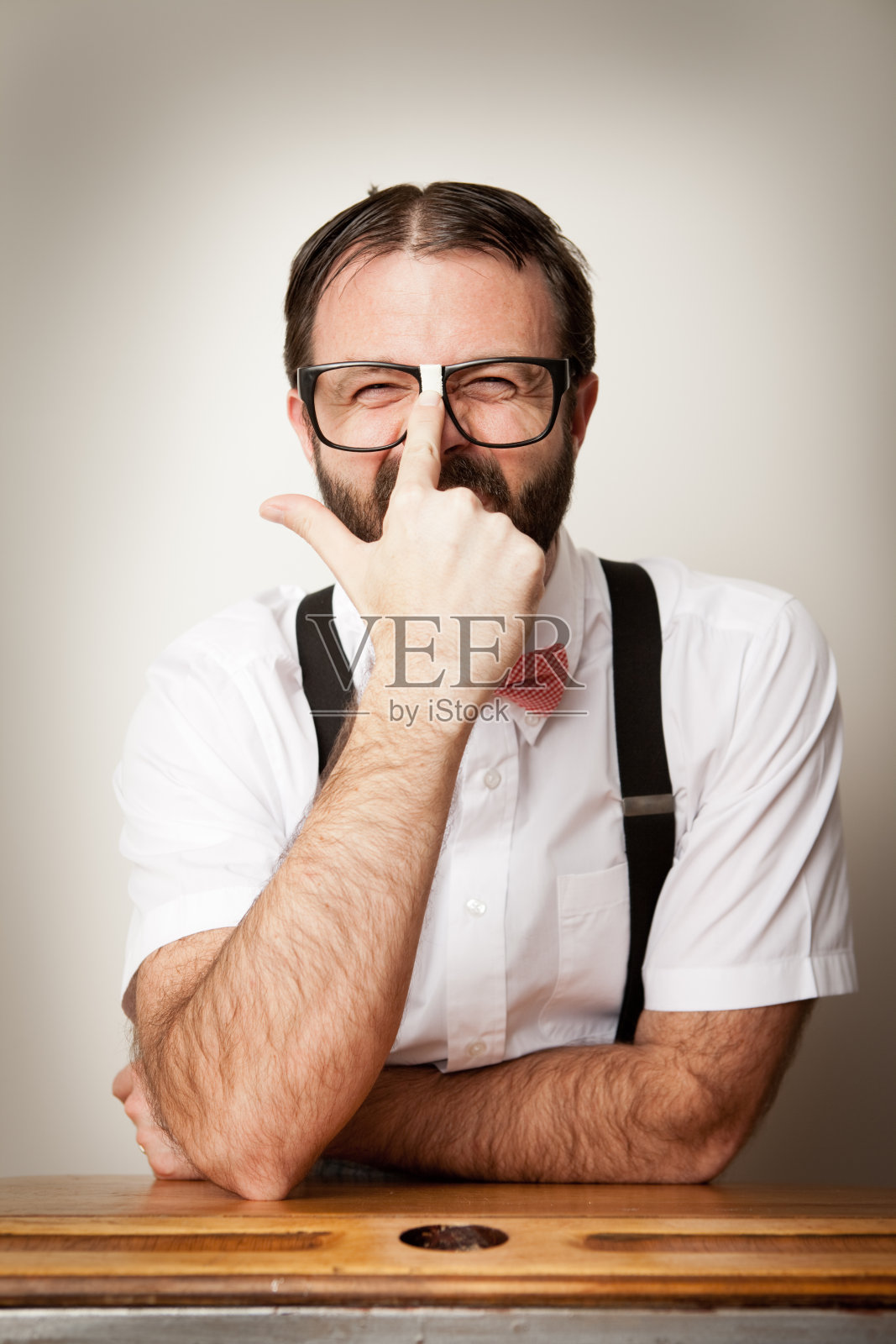 书呆子坐在办公桌前,抬高他的眼镜照片摄影图片