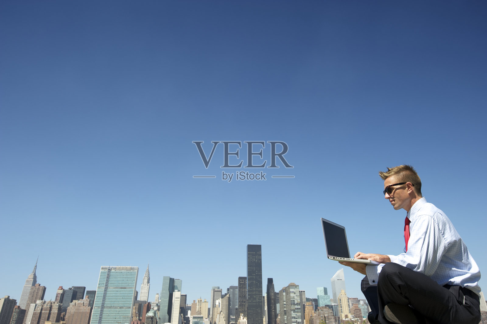 戴着太阳镜的商人在城市天际线的笔记本电脑上打字照片摄影图片