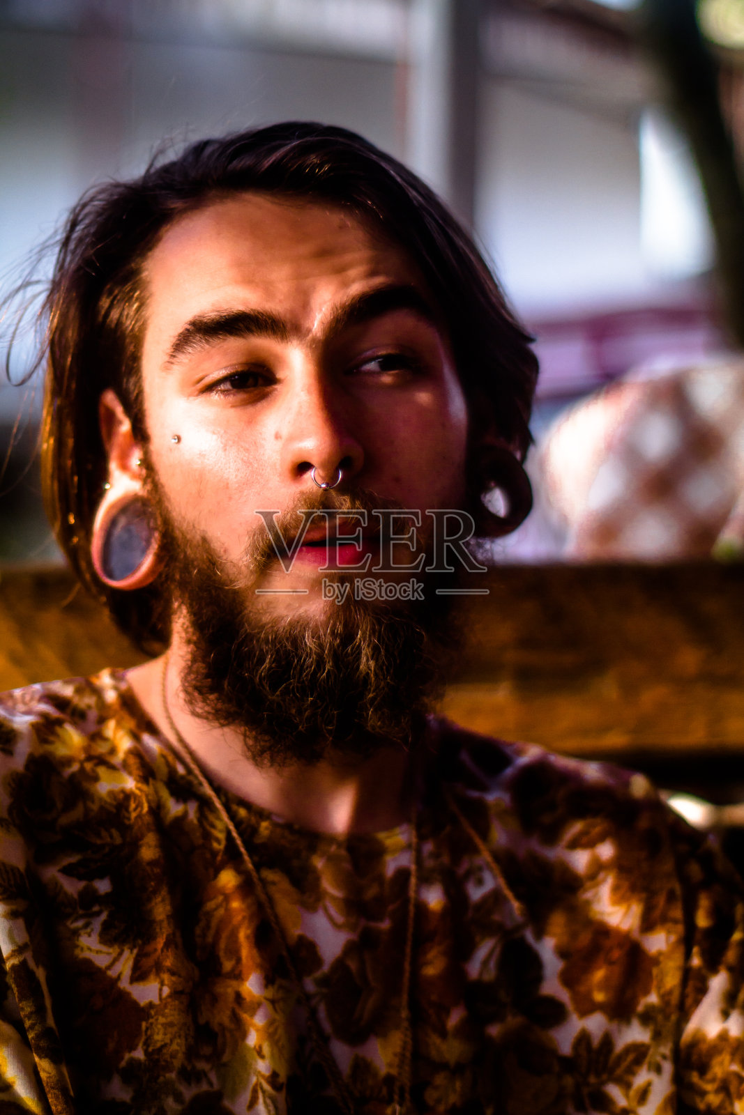 一个年轻男子的脸肖像与胡子和棕色头发,鼻子穿孔和异国情调的耳环拍摄在黄昏照片摄影图片