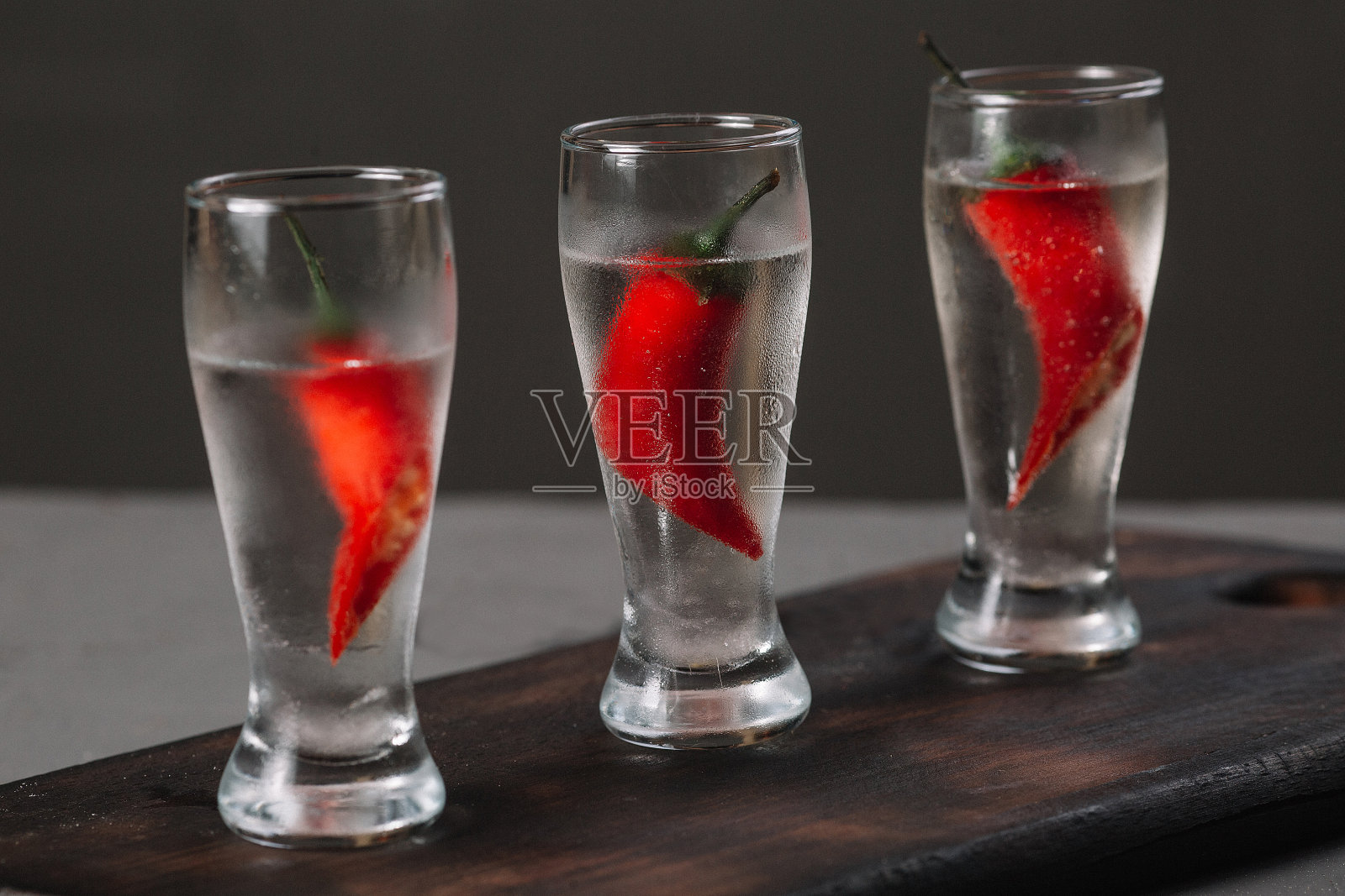 深色背景下的木砧板上,用小酒杯盛着冰凉的伏特加照片摄影图片