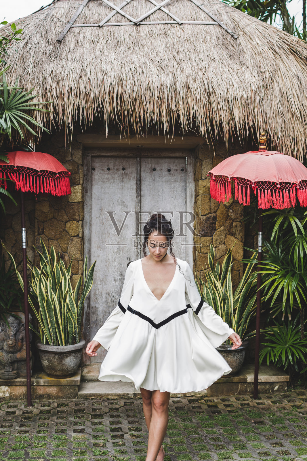 乌布村身穿白袍的年轻女子,有着传统的巴厘建筑。巴厘岛的房子风格。时尚风格,卷发,轻装。别墅在Changgu照片摄影图片