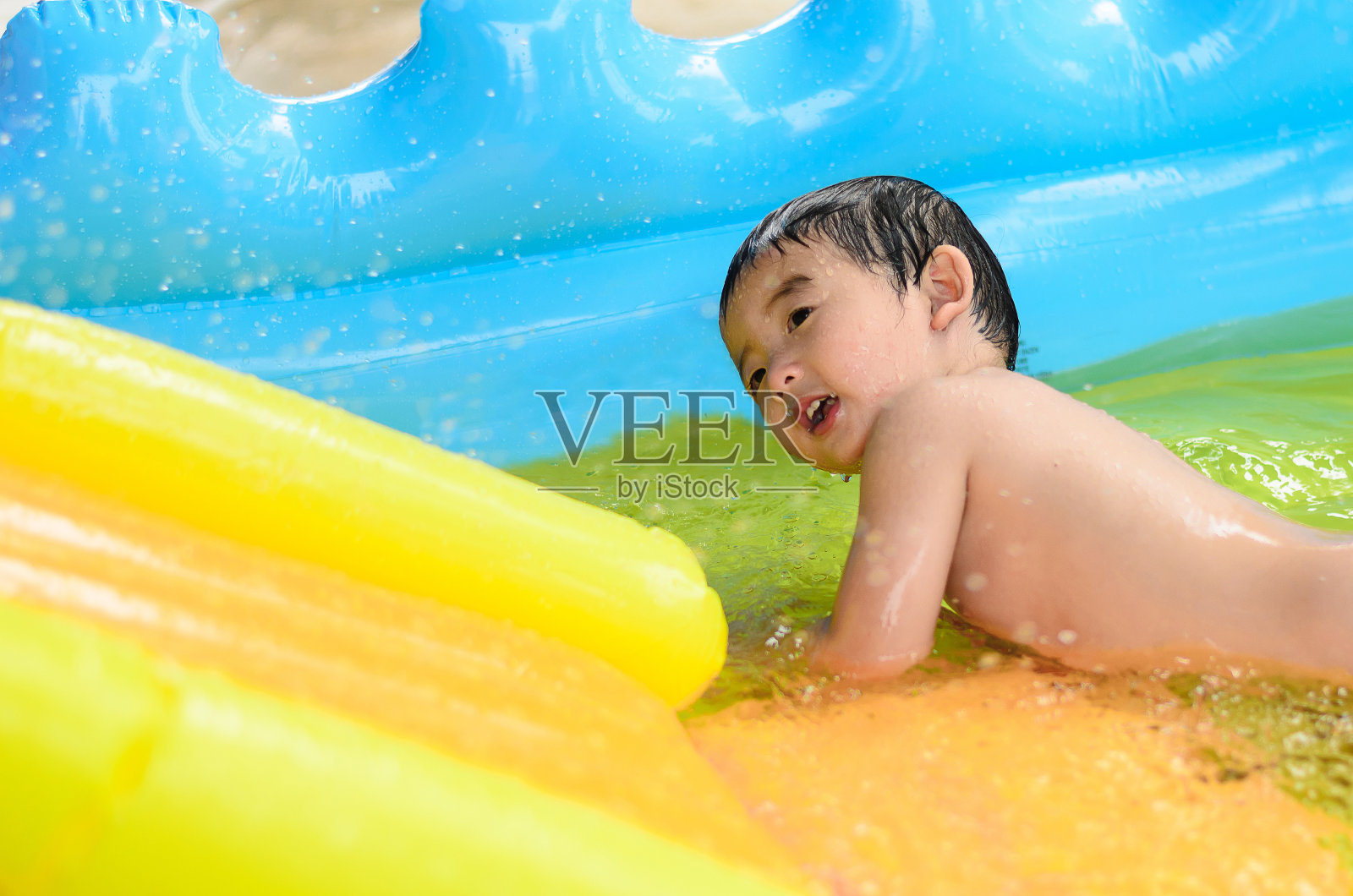亚洲孩子在充气婴儿池,水和玩具。照片摄影图片