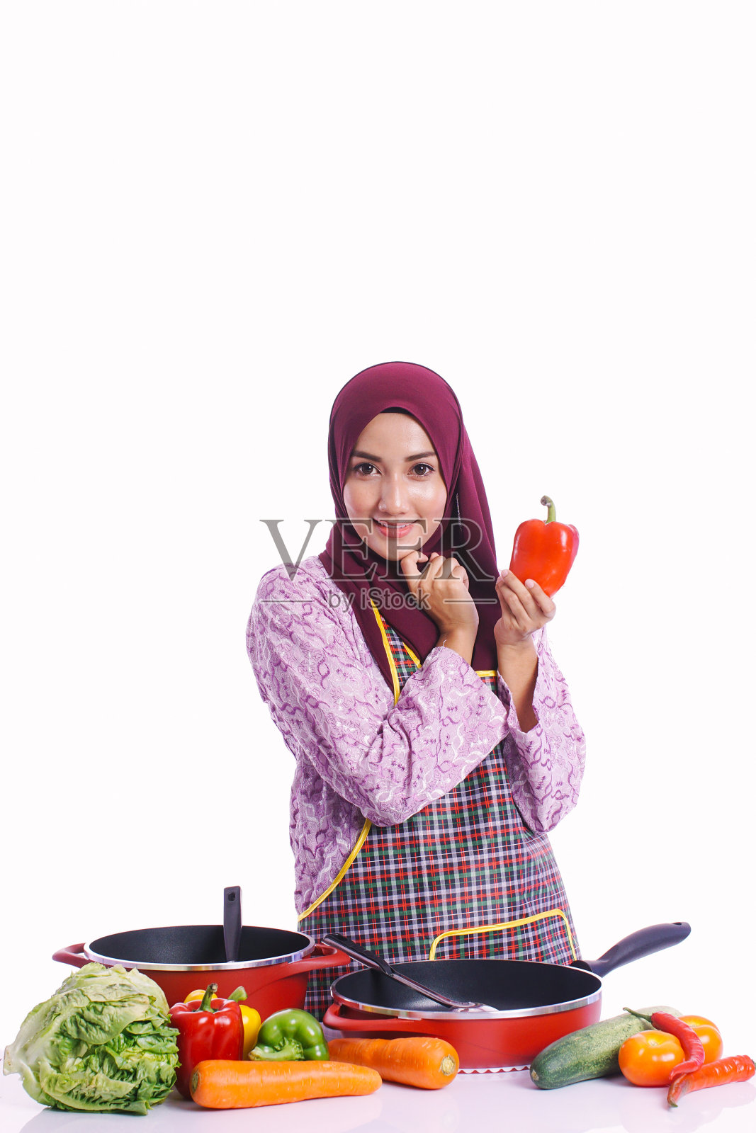 家庭主妇穿着围裙,选择红辣椒,用不同的姿势烹饪,在白色的背景孤立-厨房,食物和烹饪概念照片摄影图片