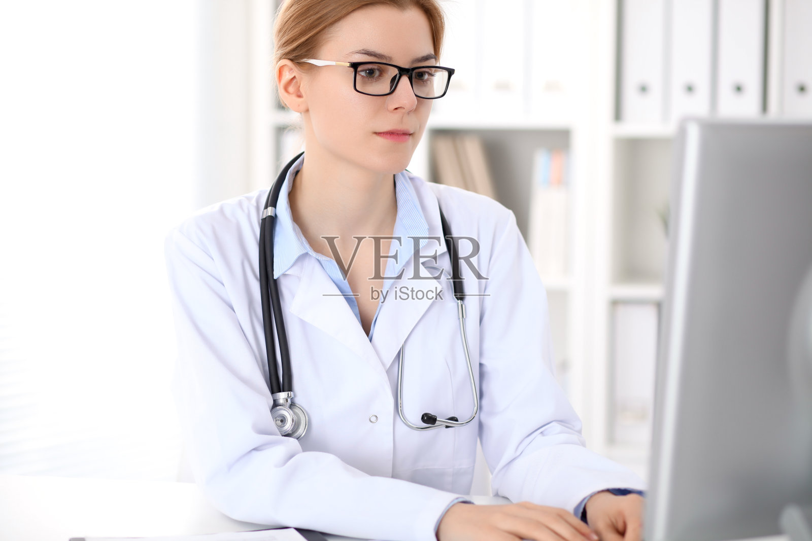 年轻的褐发女医生坐在桌子和工作在医院的办公室。照片摄影图片