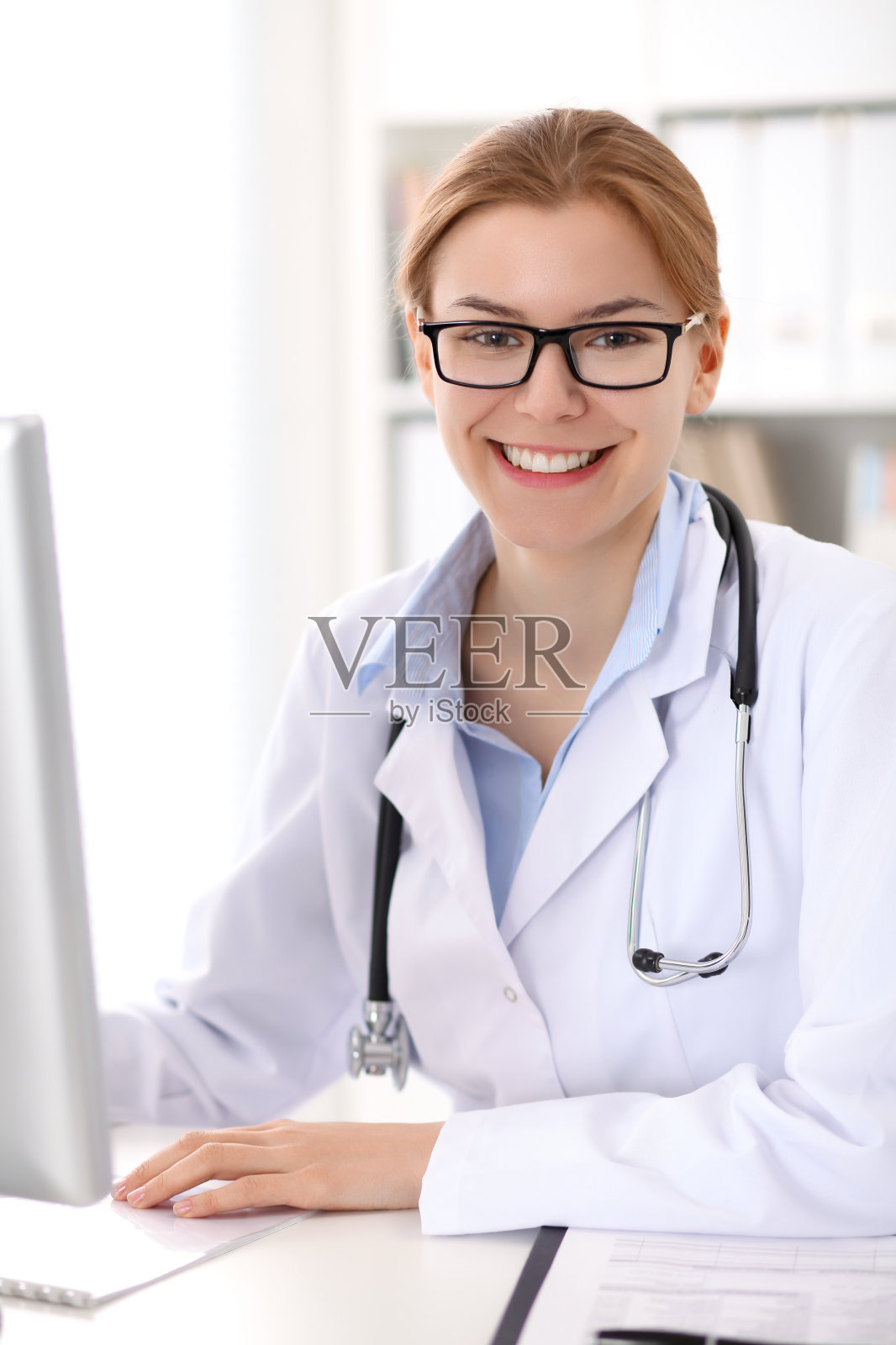 年轻的褐发女医生坐在桌子和工作在医院的办公室。照片摄影图片