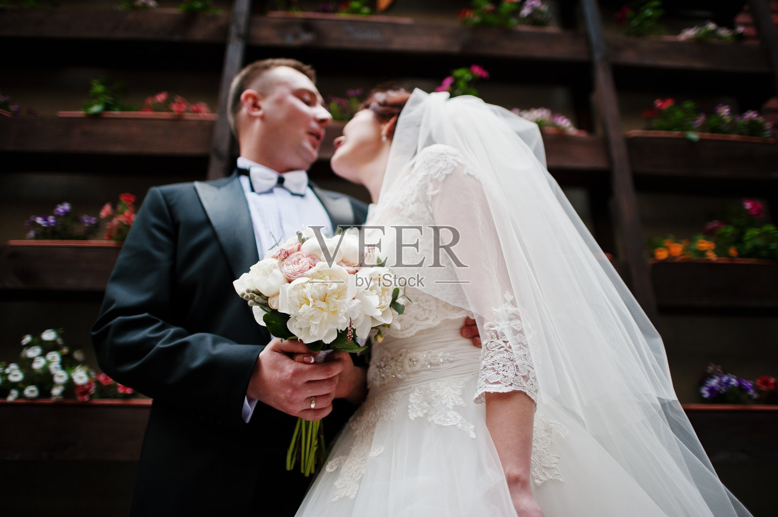 美丽的新婚夫妇留在背景墙与盆花。照片摄影图片