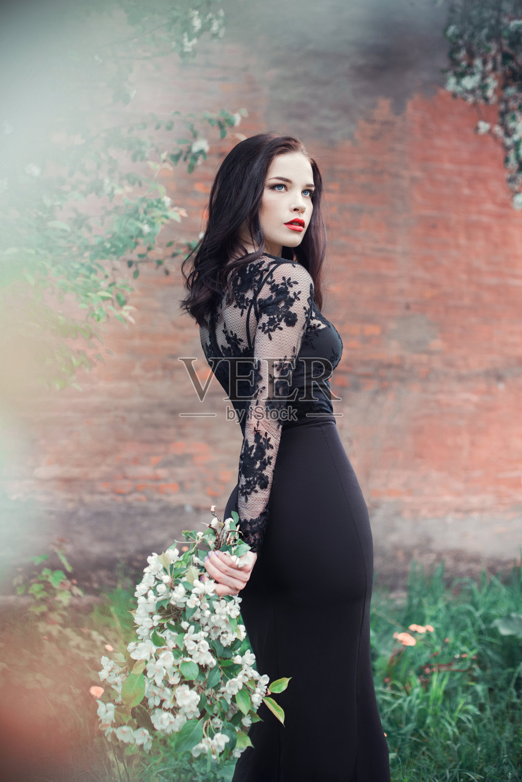 时尚艺术女人在夏天附近开花的苹果树,亮闪闪的口红。春夏季心情,神秘浪漫的女孩形象在一棵黑色连衣裙的花。女人的梦想照片摄影图片