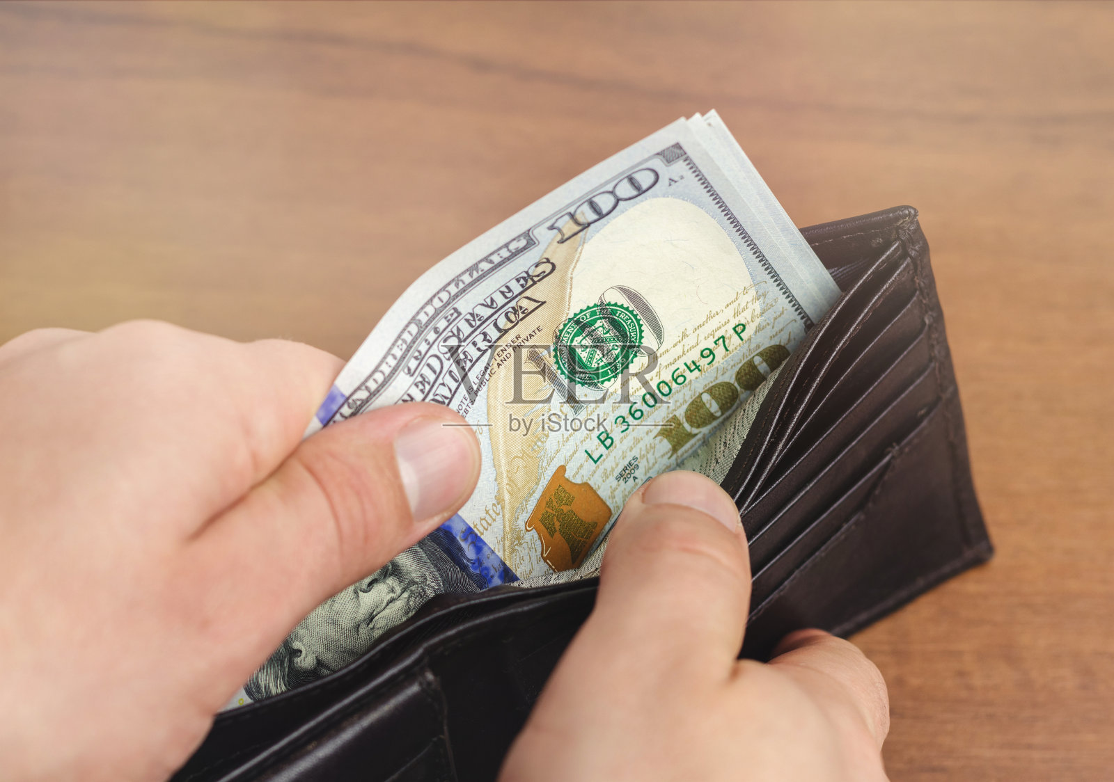 特写的男性手拿百元钞票钱包,木制背景,货币和金融概念。照片摄影图片