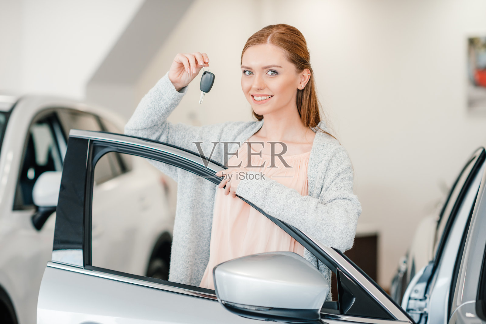 快乐的女人拿着车钥匙,站在汽车经销商沙龙照片摄影图片