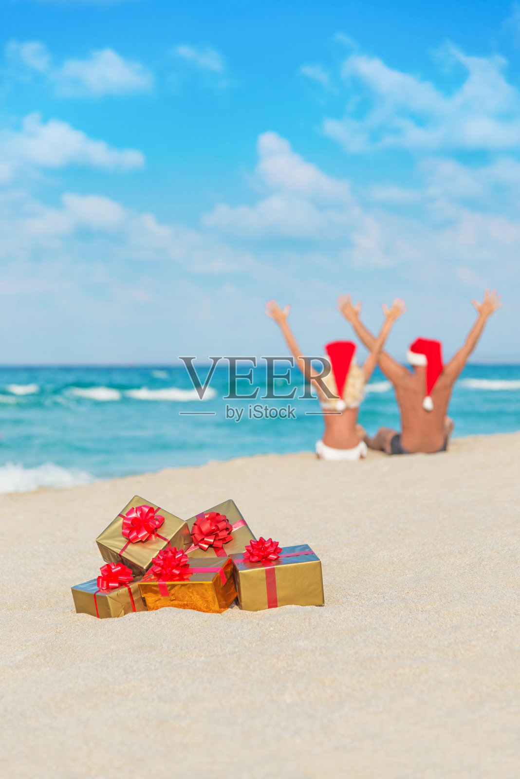 新婚夫妇戴着圣诞老人帽,在海滩上互赠礼物照片摄影图片