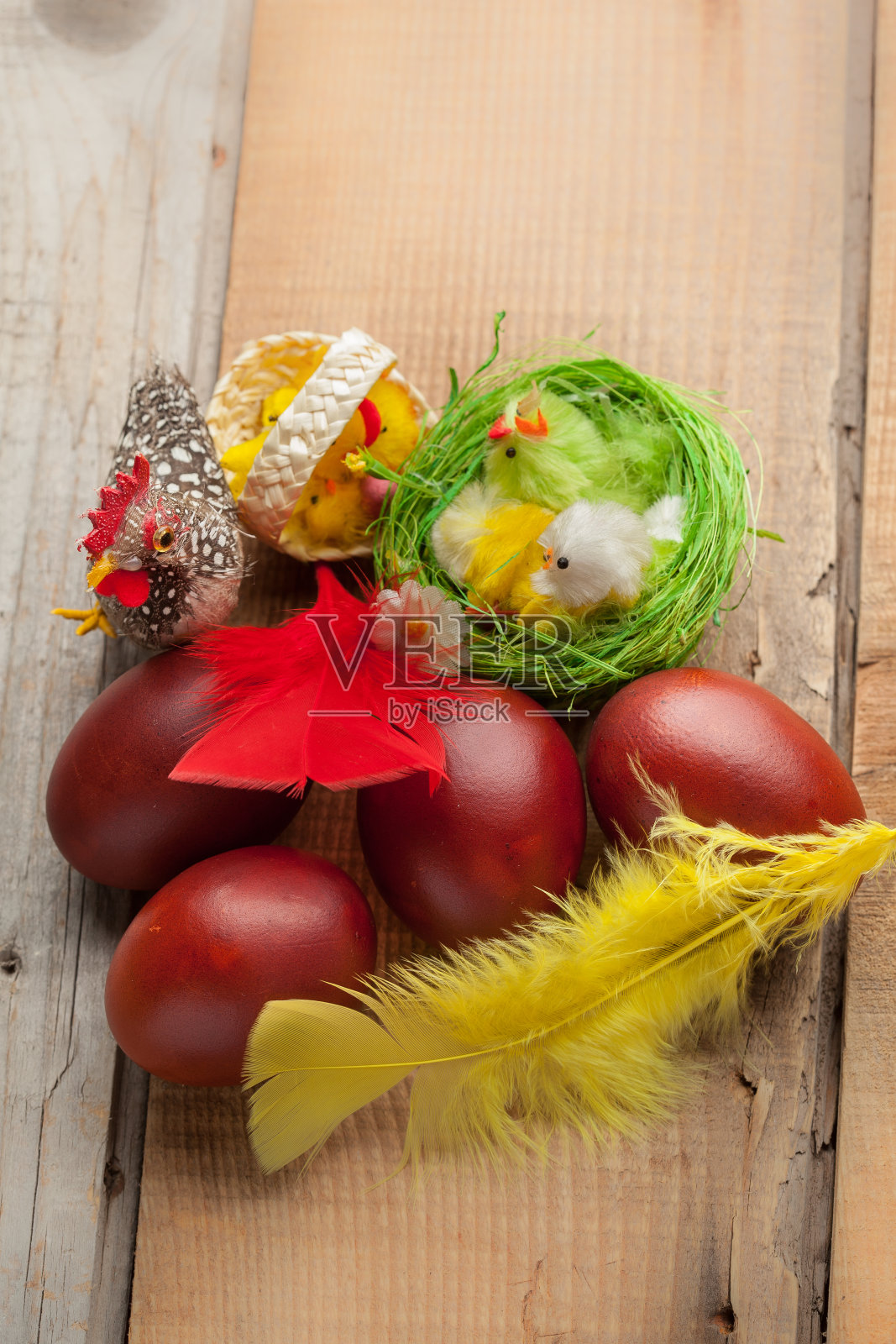 红色的复活节彩蛋放在有羽毛和鸡的旧木桌上照片摄影图片