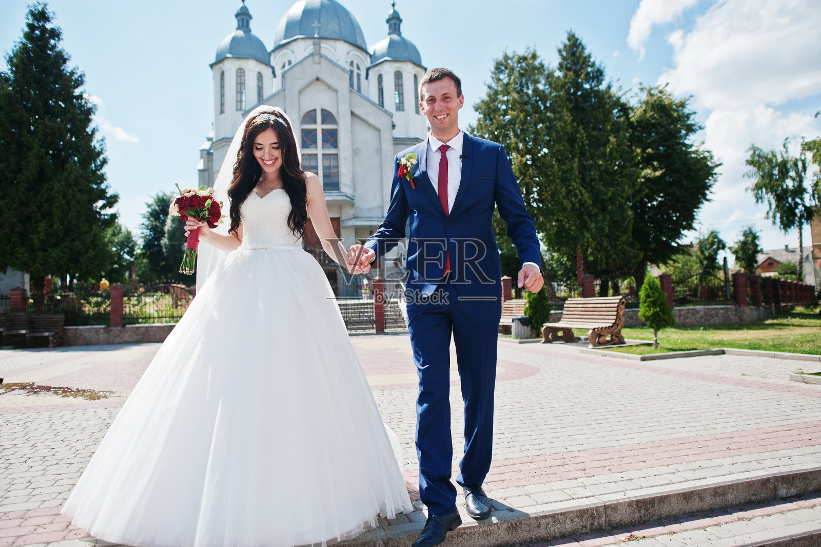 在阳光明媚的日子里,一对快乐的新婚夫妇在教堂附近。照片摄影图片