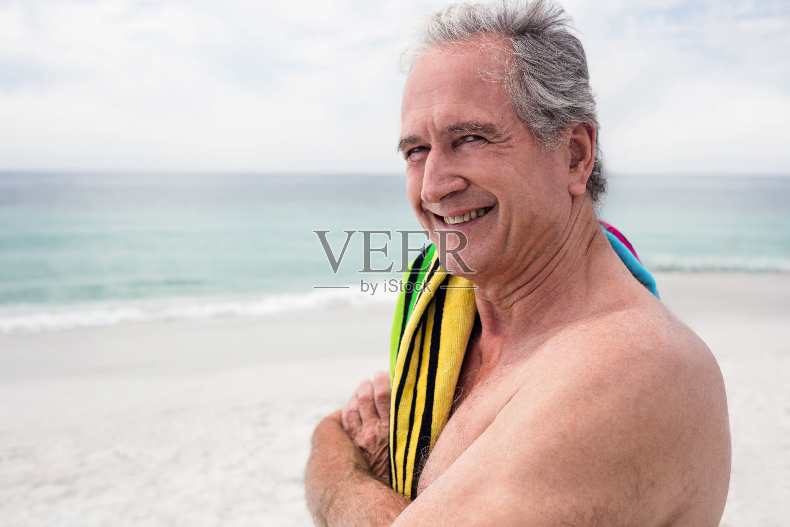 快乐的老人站在沙滩上,肩上扛着毛巾照片摄影图片