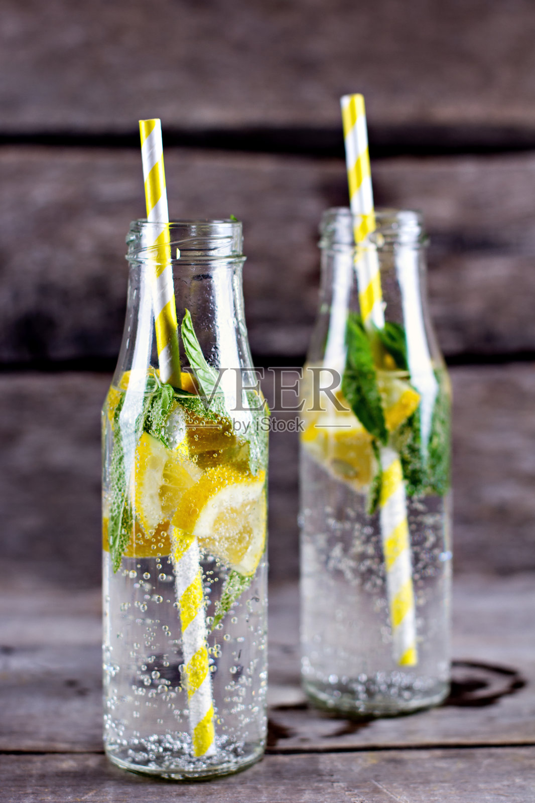 木桌上放着装有柠檬和薄荷的水瓶。照片摄影图片