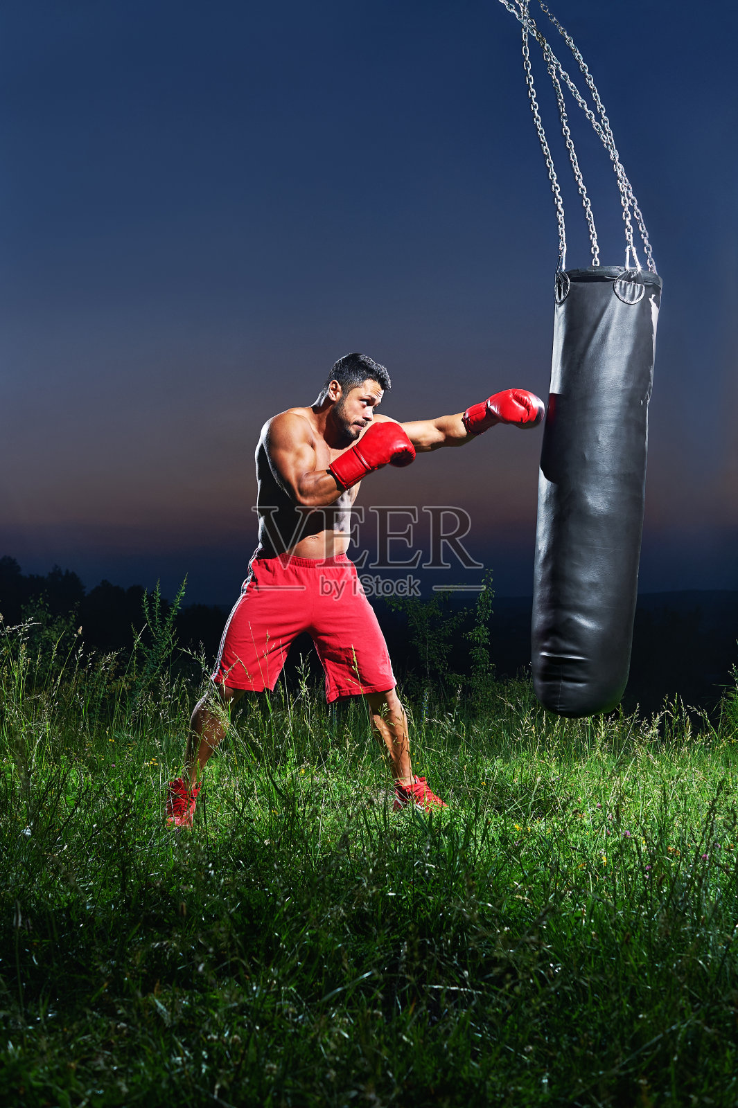 年轻英俊的男拳击手在户外练习沙袋照片摄影图片