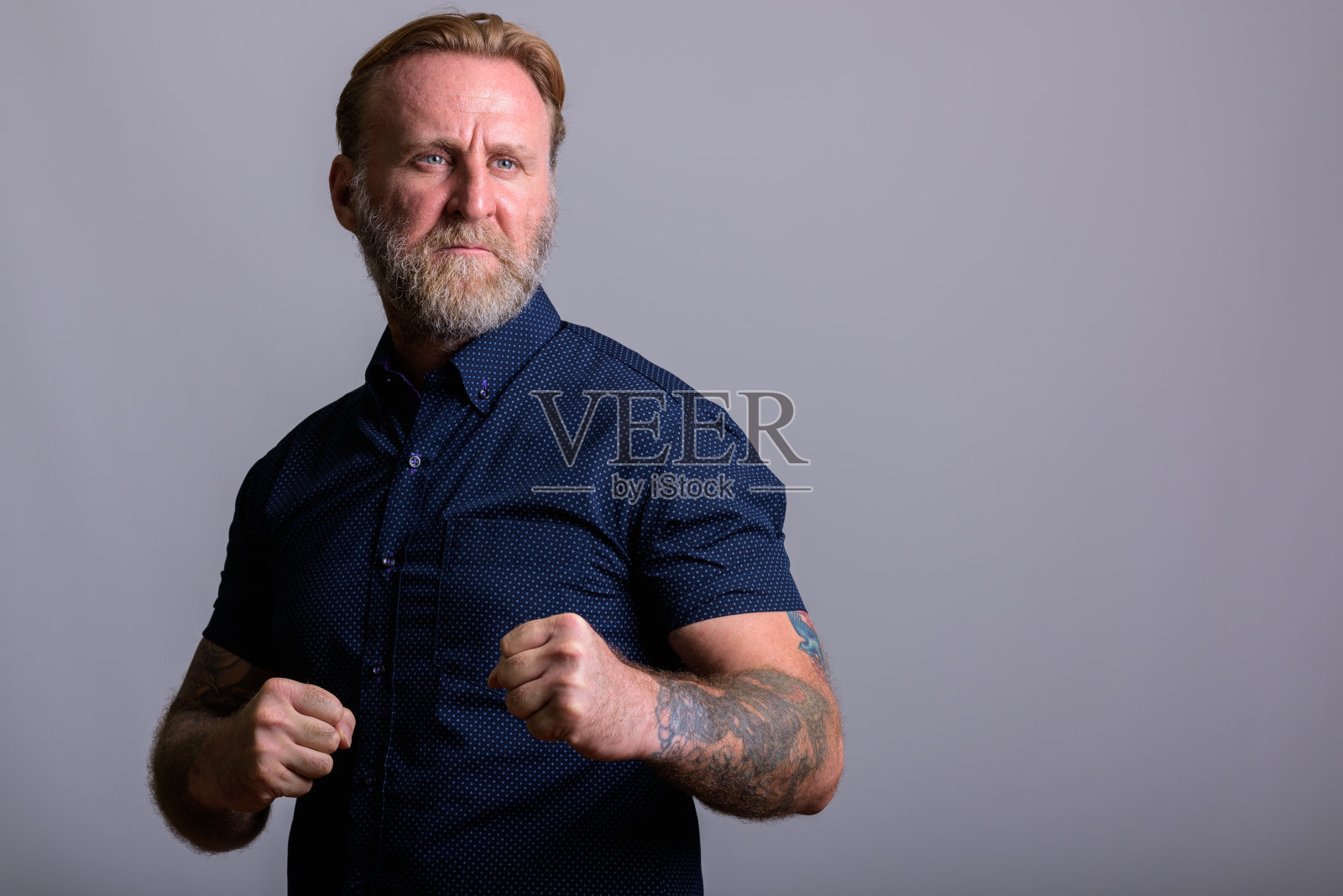 在灰色的背景下,一名手纹身的大胡子男子举起双拳思考照片摄影图片