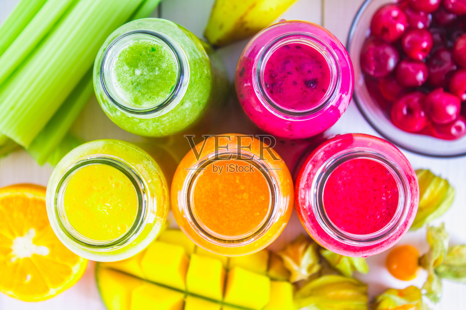 木桌上放着各种颜色的冰沙,有芒果、橘子、香蕉、芹菜、浆果。照片摄影图片