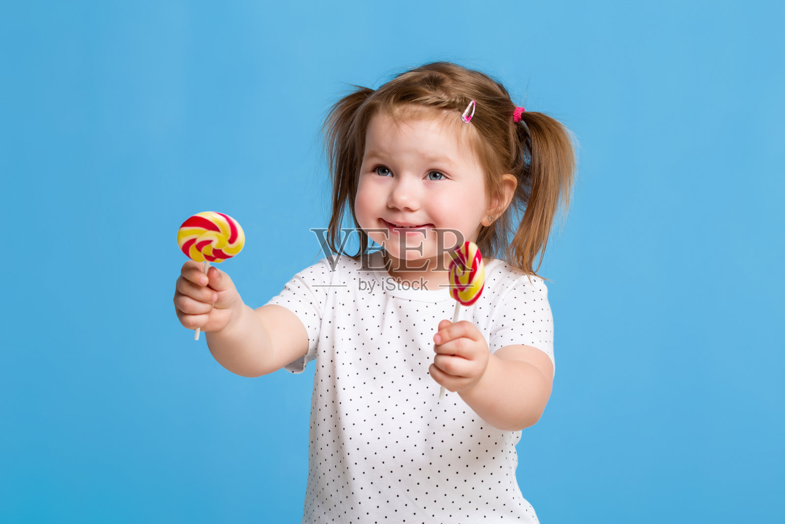 美丽的小女孩拿着巨大的螺旋形棒棒糖,在蓝色的背景上快乐地微笑着照片摄影图片
