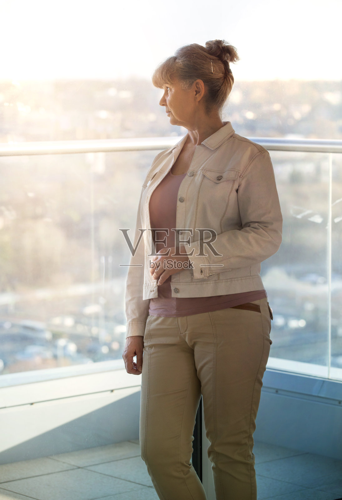 退休年龄好看的女人对着窗户和城市景观。照片摄影图片