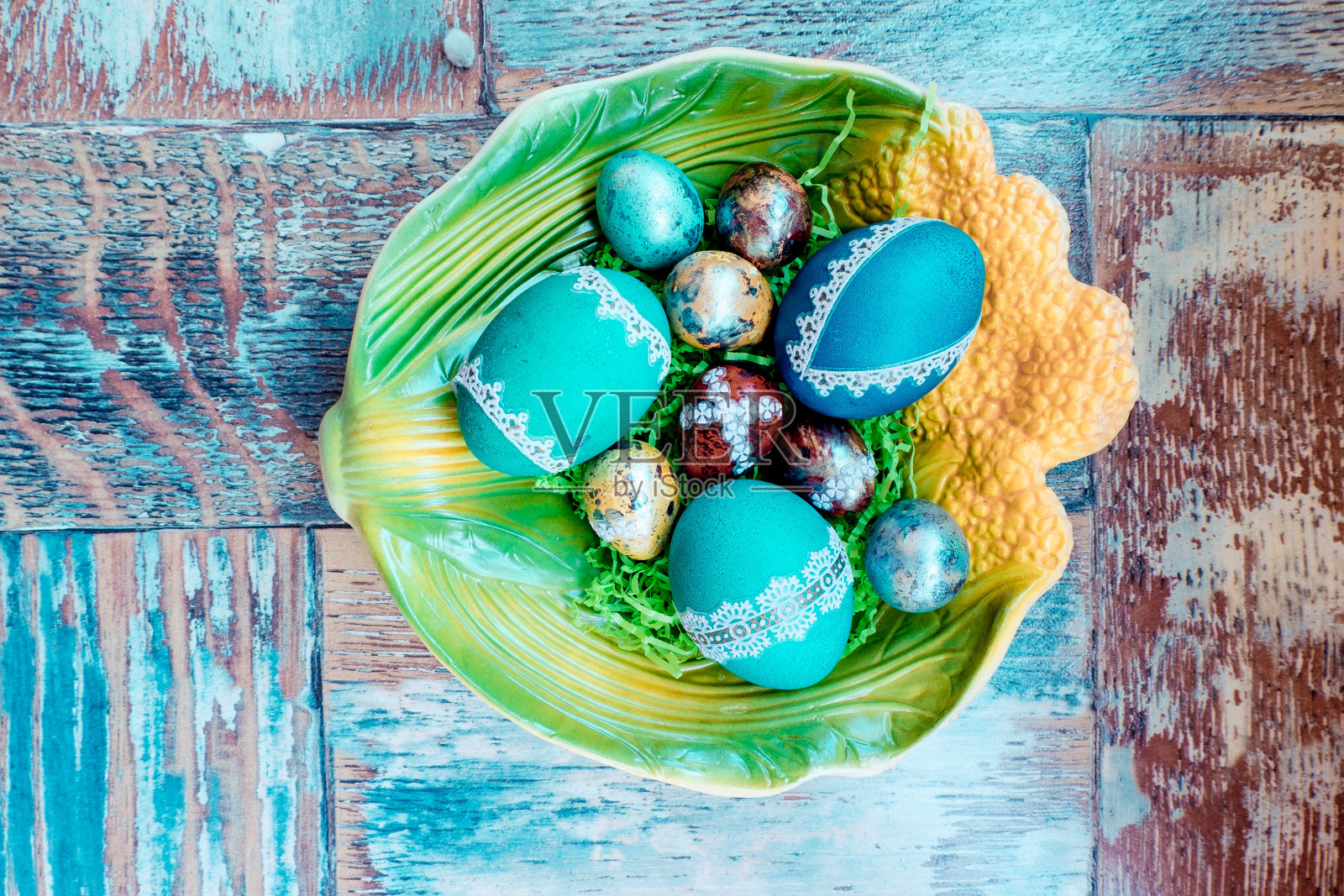 在那张破旧的旧木桌上,有一个盘子,上面画着各种颜色的复活节彩蛋和羽毛、柳条照片摄影图片